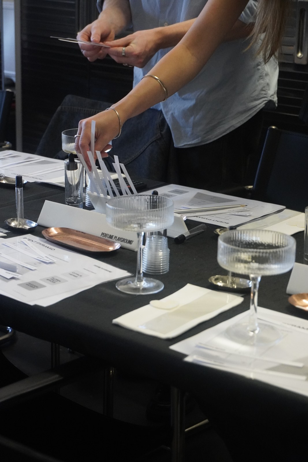 A participant working with glassware and botanical essences at a perfume-making table.